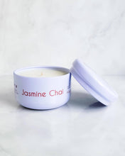 Load image into Gallery viewer, Infusion Candle Co. Jasmine Chai soy travel candle in a white tin container with a matching lid, displayed on a marble surface. The candle label reads 'Jasmine Chai, Floral Tea Blend,' showcasing the compact and portable design of this 4 oz candle, perfect for travel. The handcrafted candle, made in Illinois, combines the sweet and floral scent of jasmine with the exotic spice of chai, ideal for bringing a touch of luxury and relaxation on the go.