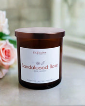 Load image into Gallery viewer, An elegant amber jar candle from Infusion Candle Co., labeled 'Sandalwood Rose' with rich notes of rose and woody sandalwood. The candle is beautifully displayed next to delicate pink roses, highlighting its floral and earthy fragrance. This soy wax candle, handmade in Illinois, brings a harmonious blend of soothing rose and warm sandalwood, perfect for creating a serene and calming atmosphere. Sandalwood Rose candle by Infusion Candle Co
