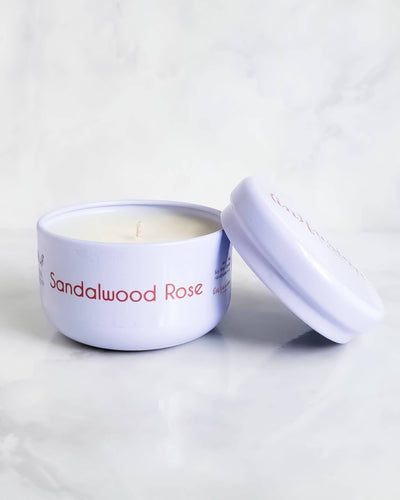 A compact white travel tin candle from Infusion Candle Co., labeled 'Sandalwood Rose' featuring a blend of rose and woody sandalwood scents. The candle is displayed with its lid partially open, showcasing the smooth soy wax. This portable candle, handmade in Illinois, provides a calming floral and earthy aroma, perfect for taking a serene and relaxing atmosphere wherever you go. Sandalwood Rose travel tin candle by Infusion Candle Co.